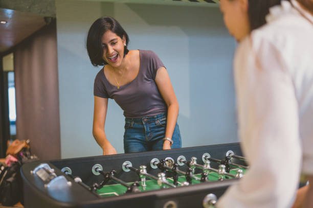 An Asian women playing table soccer indoor game in the co-working office during break time to relieve stress from work.