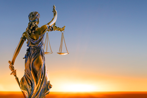 A statue of lady justice looking out towards a rising sun.