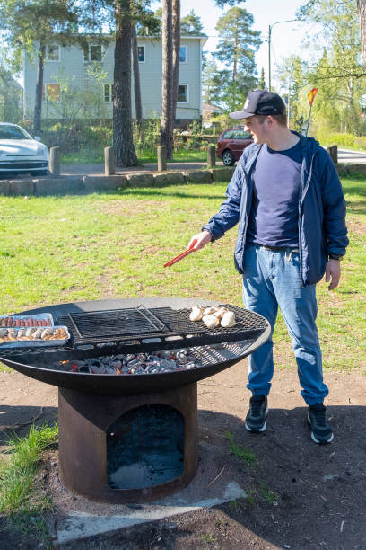 der mann bereitet essen auf dem grill zu. freizeitaktivitäten auf der straße am wochenende. finnland grillplatz im stadtpark. - barbecue grill broiling barbecue vegetable stock-fotos und bilder