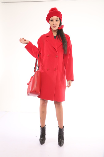 young beautiful woman in red coat holding bag front of white background. studio shot. white background. fashion shot. raw photo.