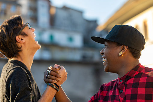 Two young men sharing a good joke laughing together and clasping hands in happy camaraderie outdoors in an urban street in close up