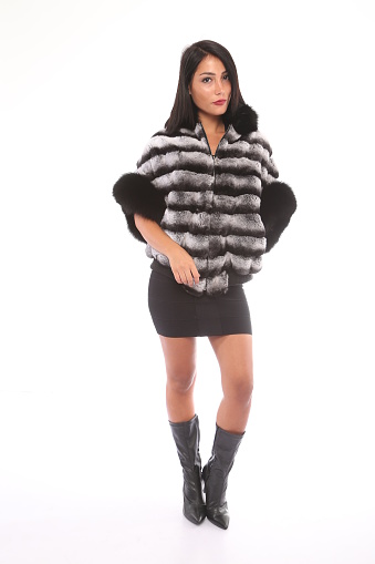 young beautiful woman in black and white fur and black boots front of white background. studio shot. fashion shoot. raw photo.