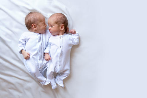 Newborn twins on the bed, in the arms of their parents, on a white background. Life style, emotions of kids
