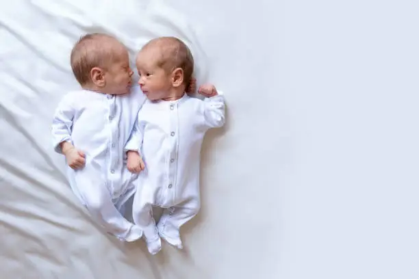 Photo of Newborn twins on the bed, in the arms of their parents, on a white background. Life style, emotions of kids