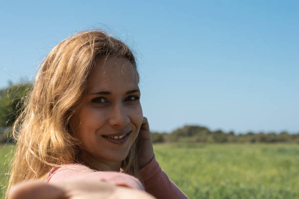 istock Cheerful young female smiling and looking at camera while taking selfie on blurred background of grassy meadow and cloudless sky 1318498259