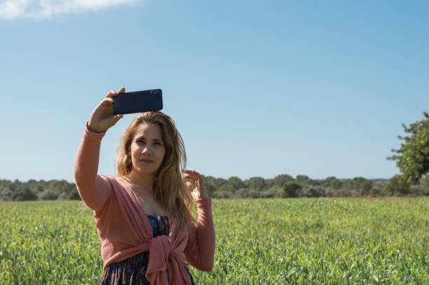istock Glad young female smiling and looking at camera while taking selfie on blurred background of grassy meadow and cloudless sky 1318498262