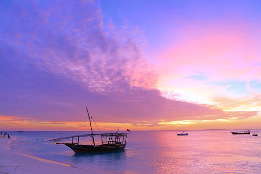 Sunset on Zanzibar. Authentic african wooden boat on the picturesque ocean shore.