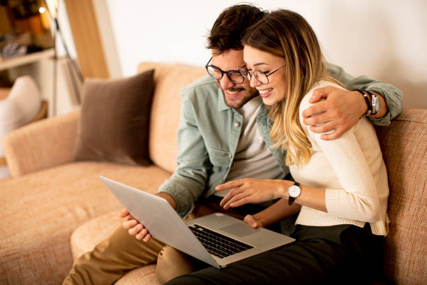 istock Young couple using laptop together while sitting on sofa at home 1318499237