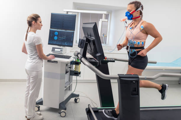 Female athlete taking a cardiopulmonary stress test in clinic Female doctor observing the progress of a cardiopulmonary stress test taken by the female athlete riding a bicycle ergometer. stress test stock pictures, royalty-free photos & images