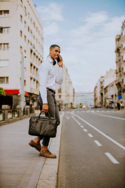 istock Young African American businessman using a mobile phone while crossing a street 1318505325