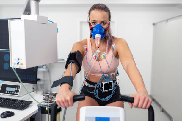 Female athlete taking a cardiopulmonary stress test in clinic Portrait of female athlete cycling on the ergometer and doing a cardiopulmonary test in clinic. stress test stock pictures, royalty-free photos & images
