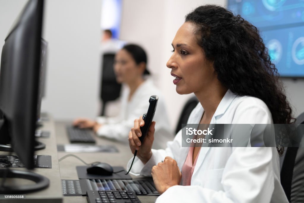 Female radiologist speaking into a dictation recorder while looking at MRI scan Female radiologist talking into the dictation recorder while looking at the MRI scans on his computer. Desk Stock Photo