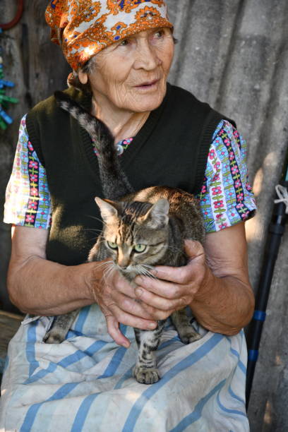 伝統的な田舎のヘッドスカーフで笑顔の先輩女性80歳の肖像画とラップの上にタビー猫を保持 - female 80 plus years vertical people ストックフォトと画像
