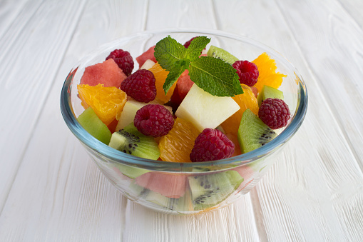 Fruit  salad in the glass bowl on the white wooden background. Close-up.