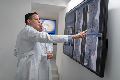 Side view of two male radiologists analysing the MRI scans on the lightbox.