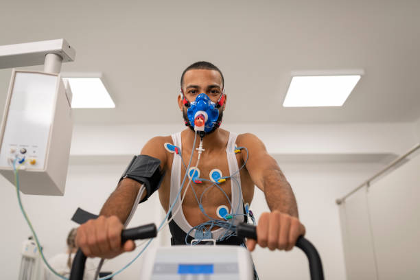 Mid adult man taking a cardiopulmonary stress test in clinic Portrait of male athlete cycling on the ergometer and doing a cardiopulmonary test in clinic. stress test stock pictures, royalty-free photos & images