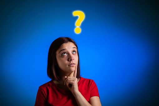 Portrait of young Caucasian woman thinking. Question mark standing over her head. Blue background.