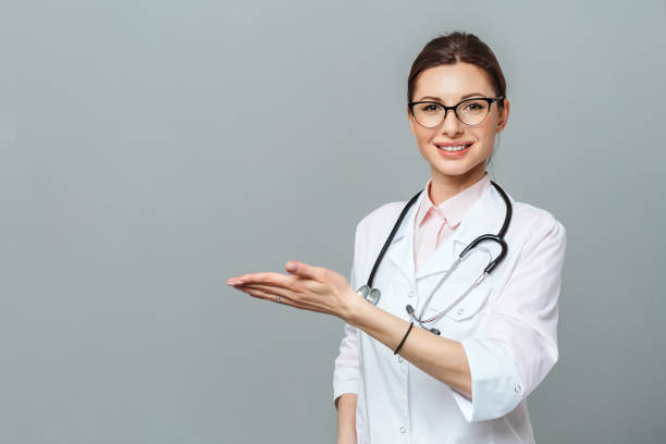 amable joven doctora sonriente. apuntando a mano al espacio de copia. aislado sobre un fondo gris - medicinal object fotografías e imágenes de stock