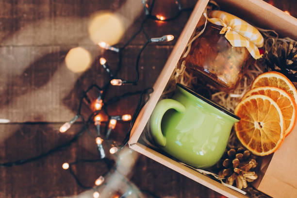 istock Gift box with tea set. Tea, cup, jam, spices, dried oranges in box with christmas lights, top view 1318513389