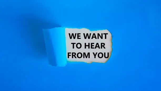 Photo of Support symbol. Concept words 'we want to hear from you' appearing behind torn blue paper. Beautiful blue background. Business and support concept.