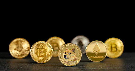 Clarksburg, MD, USA 05-15-2021: Symbolic cryptocurrency types represented as shiny coins are lined up against dark background. Among them dogecoin which started as a joke is currently gaining popularity