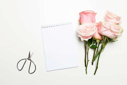 Scissors, notepad and roses on white table.