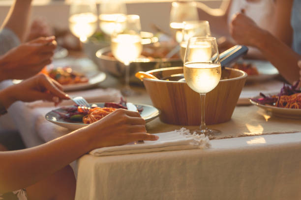 Friends enjoying a meal together on a table at sunset. Friends enjoying a meal together on a table at sunset. There is spaghetti Bolognese  and salad on the plates on the table. There are glasses of wine and other food on the table. Tight crop showing only food and hands outdoor dining photos stock pictures, royalty-free photos & images