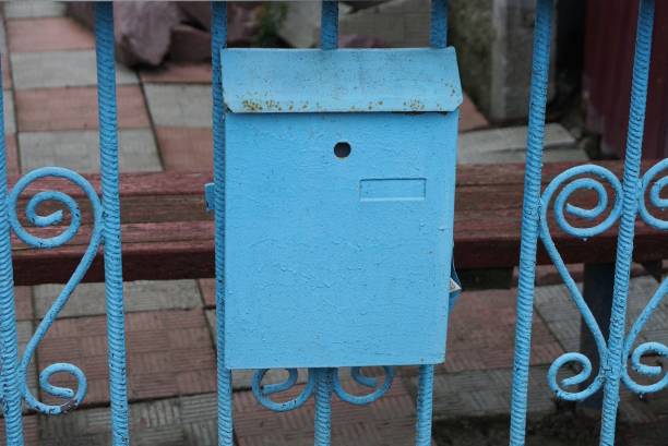 one blue metal mailbox hanging on the iron bars of the fence in the street
