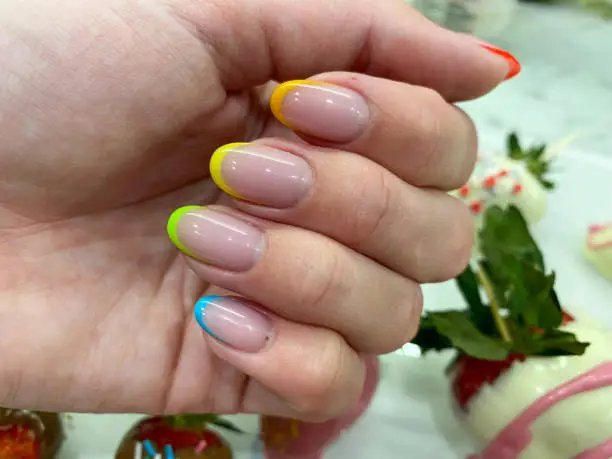 Photo of Beautiful multicolored women's manicure fashionable stylish french on the fingers with gel varnish of different colors of the rainbow transparent yellow red green blue. Stylish nail design