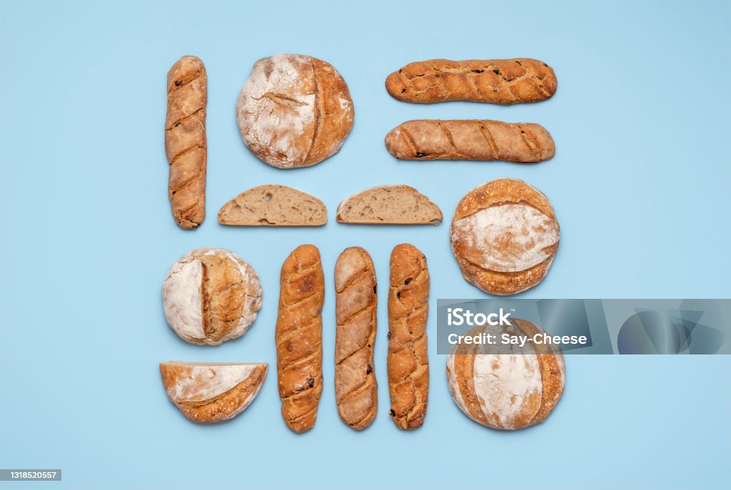Sourdough bread variety top view on a blue background. Homemade bread flat lay. Food knolling with homemade sourdough bread. Round loaves and baguettes made with sourdough arranged symmetrically on a blue background. Bread Stock Photo