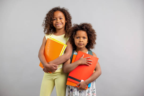 istock Mixed Race Sisters Holding Notebooks And Looking At Camera 1318524696