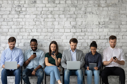 Multicultural team of gadget users sitting in line, using laptops, tablets, mobile phones, working, reading messages, chatting online on social media, watching content on internet. Copy space