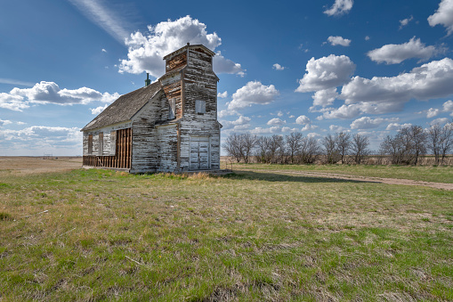 horizontal image of a quaint little white country church with a steeple sitting in a green meadow surrounded by trees under a beautiful blue sky with white clouds floating by in the summer time.