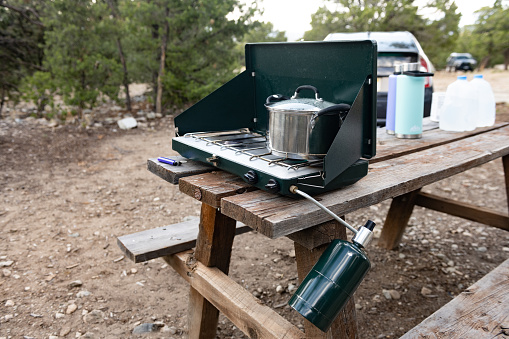 This is a photograph of a propane gas camping stove setup on a picnic table at a campsite near Great Sand Dunes National Park during summer in Colorado, USA.