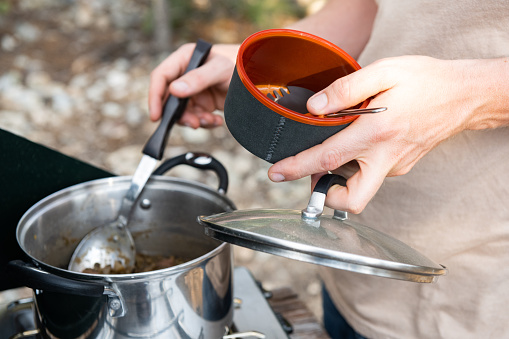 This is a close up photograph of the hand’s of a Caucasian man in his 30s cooking with a camping stove at a campsite near Great Sand Dunes National Park during summer in Colorado, USA.