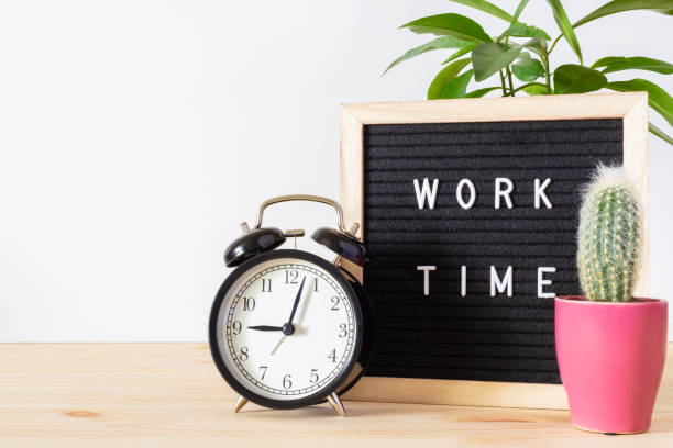 istock Classic black alarm clock, laptop and black board with words 'work time' on wooden table with white wall background and copy space. 1318560355