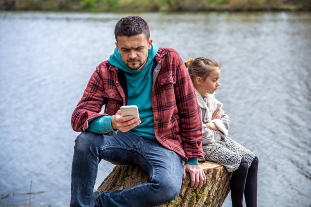 Dad with a phone in his hands does not pay attention to his little daughter. Dad is checking his phone, not paying attention to his daughter, for a walk in the woods. ignoring photos stock pictures, royalty-free photos & images