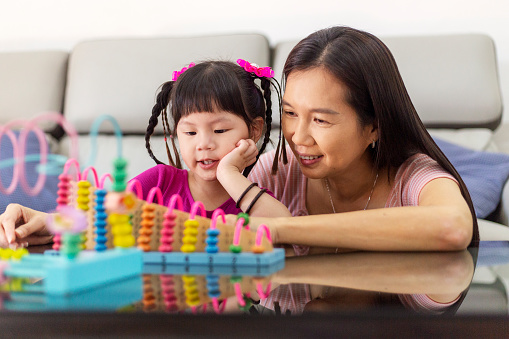little girl learning mathematics using abacus at home, mother teaching beside patiently