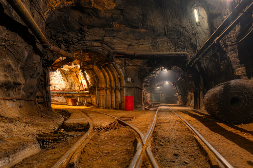 Tunnel of the mining of an underground mine. Lots of pipelines on the ceiling and rail track for trolleys.