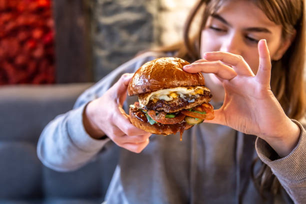 istock Big appetizing burger with meat in female hands in a cafe. 1318573451