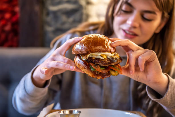 istock Big appetizing burger with meat in female hands in a cafe. 1318573454