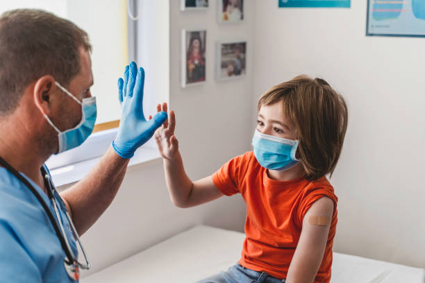 arzt und niedlicher junge geben sich nach covid-19 impfung hochfünf. kinderimpfung. coronavirus-epidemie. kopieren sie den speicherplatz. - nurse high five mask stock-fotos und bilder