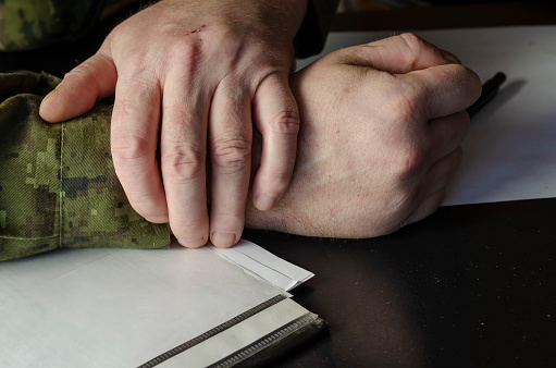 Officer's hands, document folder on black desk in close-up. A middle-aged man in a green camouflage uniform. Indoors. Selective Focus. Low key.