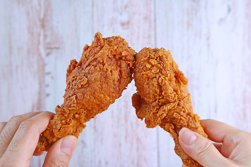 Closeup Man's Hand and Woman's Hand Clinking Crispy Fried Chicken Drumsticks Against Wooden Wall