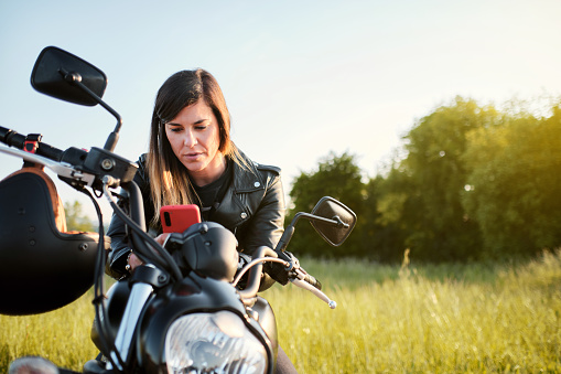 young woman using her smart phone while sitting on a motorcycle