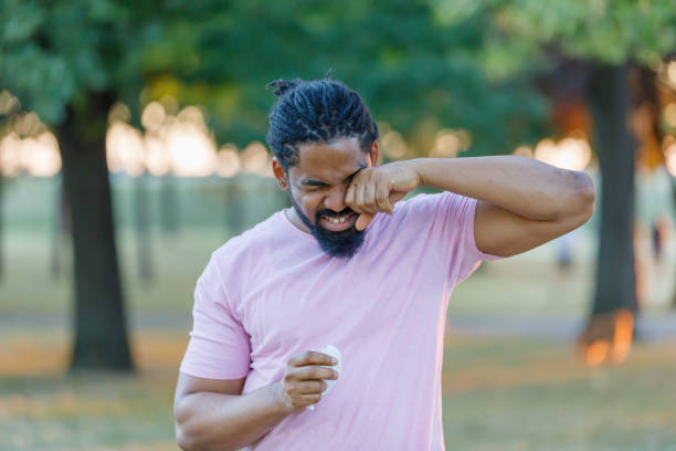 An African-American Man is Having Allergy Problems Outside in Nature. Man of African-American Ethnicity is Rubbing his Eyes Due to Problems with Sight in the Public Park. human eye scratching allergy rubbing stock pictures, royalty-free photos & images