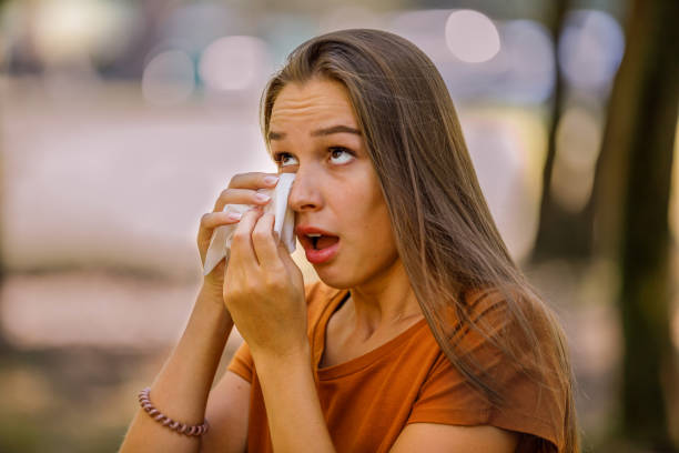 Young Woman is Having Allergy Problems Outside in Nature and Rubbing her Eyes. A Woman of Caucasian Ethnicity with Long Hairis Rubbing her Eyes with Paper Handkerchief Due to Problems with Sight in the Public Park. wiping tears stock pictures, royalty-free photos & images