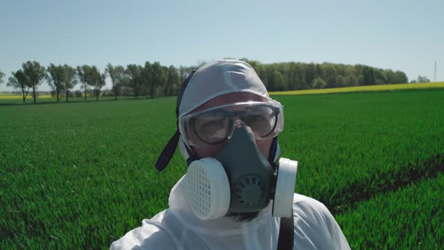 Scientist biologist in a gas mask and protective suit shows a farmland.