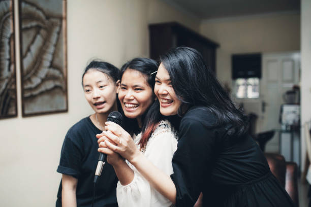 asiatica femmina canta karaoke ridendo e godendo tutti insieme nel soggiorno di casa sua - playback foto e immagini stock