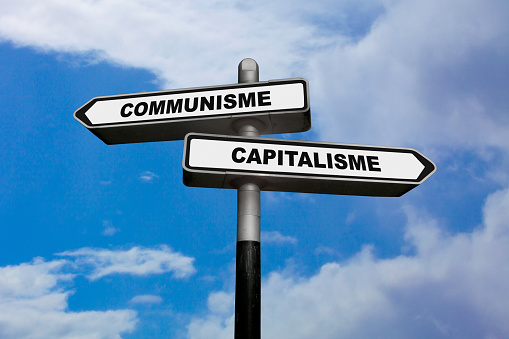 Two direction signs, one pointing left and the other one, pointing right, with written in them in French : Communisme / Capitalisme, meaning in English: Communism / Capitalism.